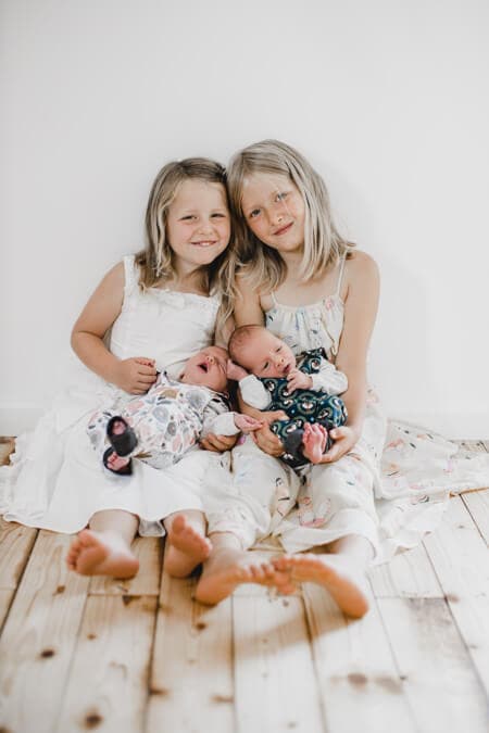 Schwester halten ihre neugeborenen Geschwister auf dem Schoß