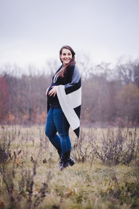 Schwangere Frau mit Strickmantel blickt über ihre Schulter