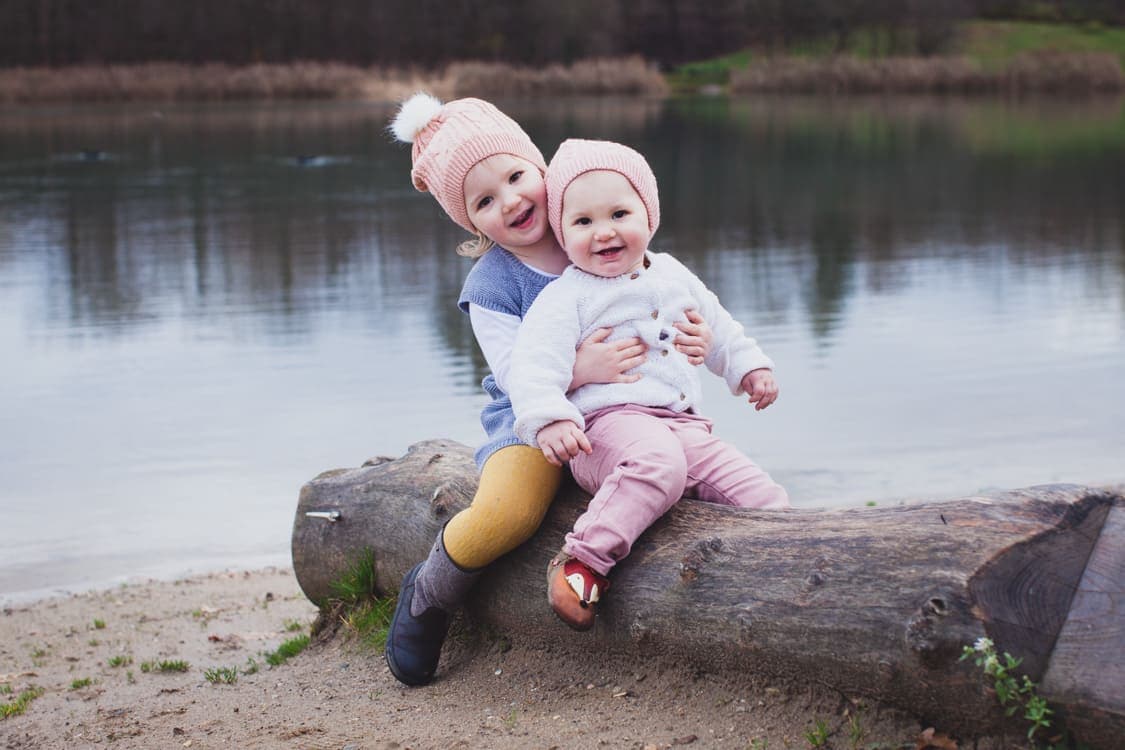 Geschwister sitzen hintereinander auf einem liegndem Baumstamm