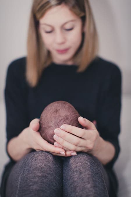 Mutter hat ihr Baby auf dem Schoß liegen und hält das Köpfchen in ihren Händen