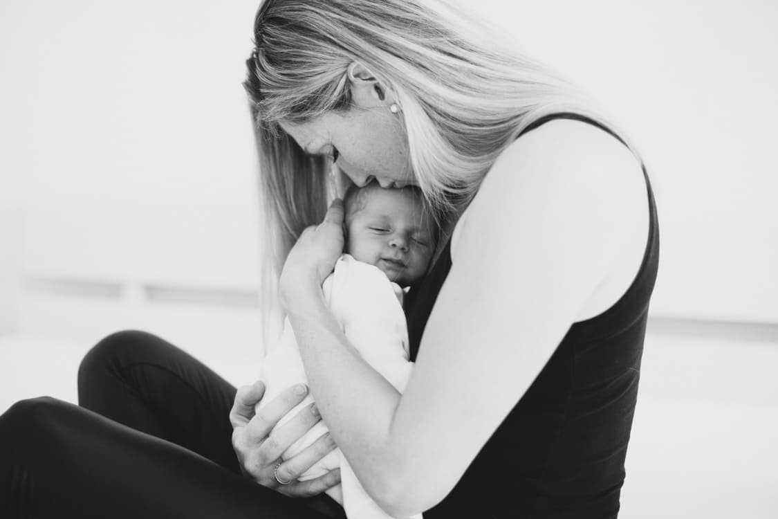 Mama küsst ihr Neugeborenes welches sie im Arm hält