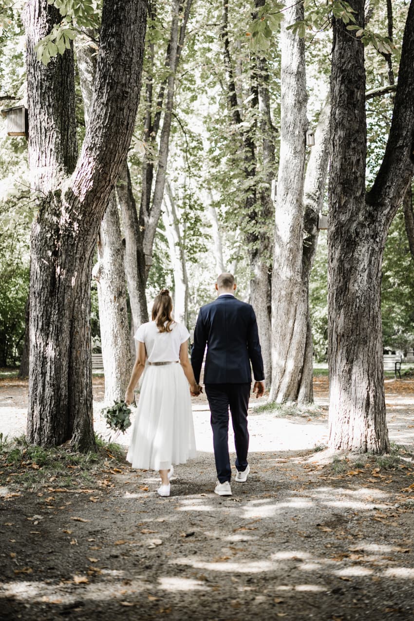 Brautpaar von hinten läuft durch eine Allee