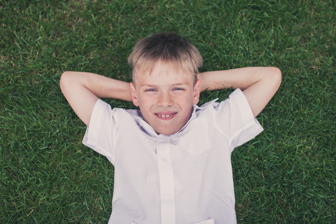 Junge liegt mit verschränkten Armen hinterm Kopf auf einer Wiese