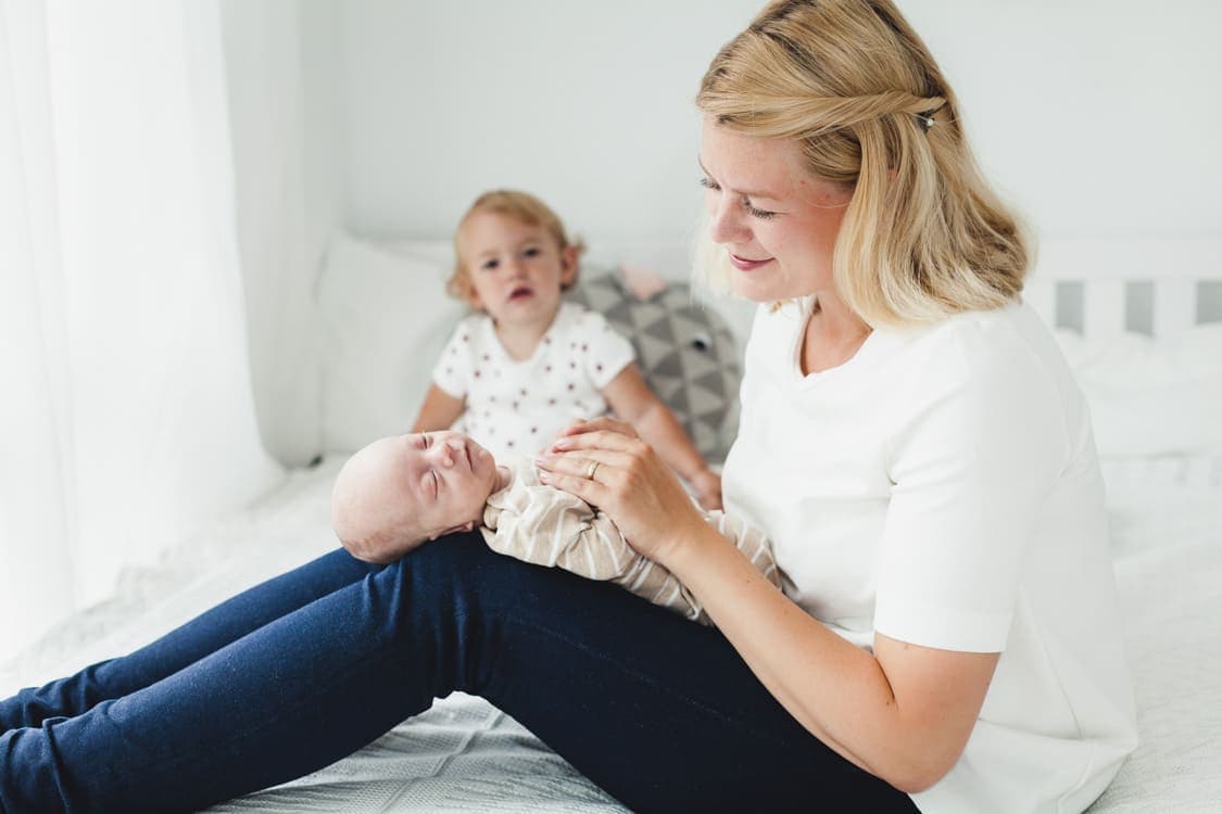 Auf dem Schoß der Mutter liegt ein Neugeborenes. Im Hintergrund sitzt die kleine Tochter.
