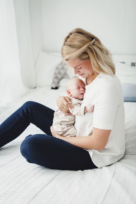 Mutter kuschelt mit Neugeborenem sitzend auf dem Bett