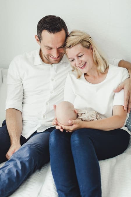 Eltern betrachten ihr Neugeborenes das vor ihnen auf dem Schoß liegt