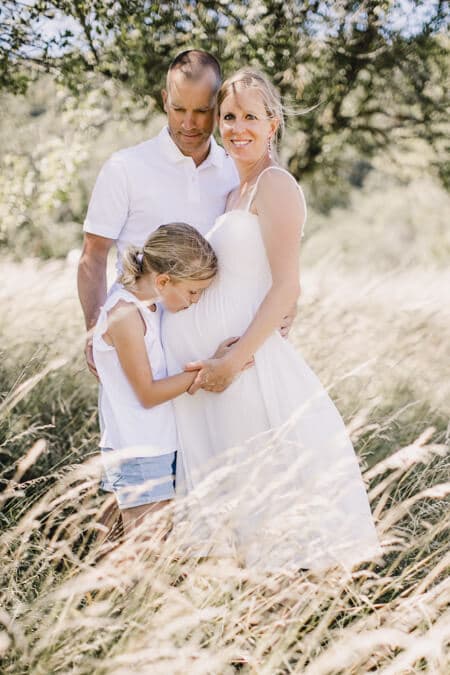 Schwangere Frau mit ihrem Mann und ihrer Tochter auf einer Wiese mit hohem Gras.