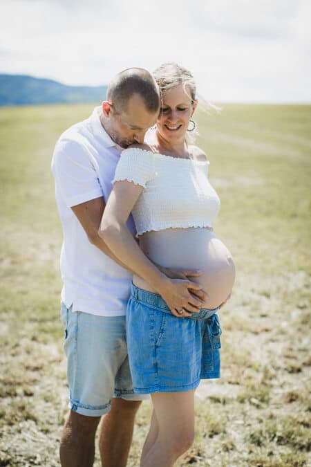 Mann umarmt seine Frau mit Babybauch von hinten