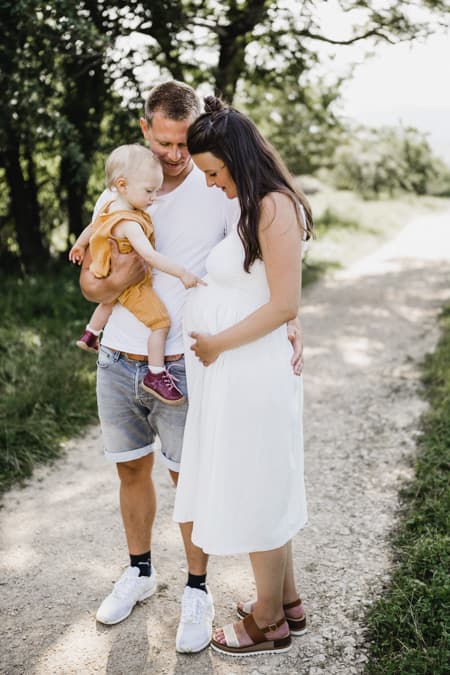 Familie mit Kind auf dem Arm zeigt auf Babybauch