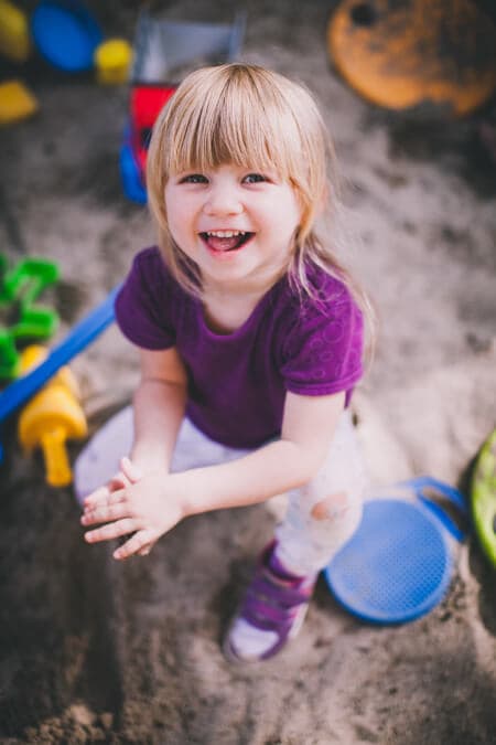 Mädchen sitzt im Sandkasten und sandelt