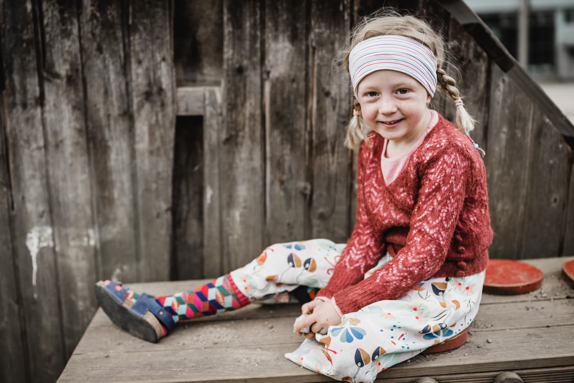 Maedchen mit Stirnband sitzt vor Holzhaus