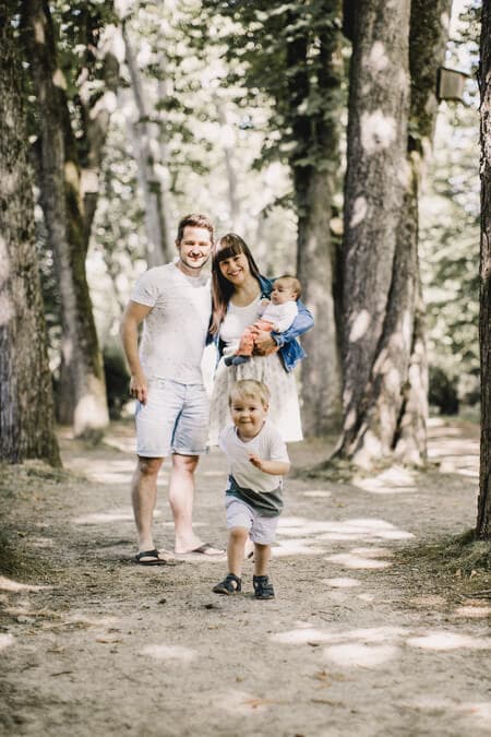Familie in einer Allee von Bäumen. Kind rennt los.