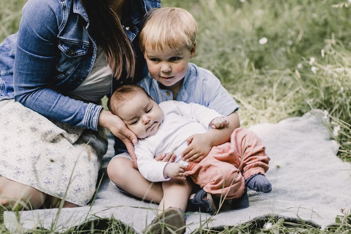 Bruder hat Baby auf dem Schoß. Die Mutter sitzt danneben.
