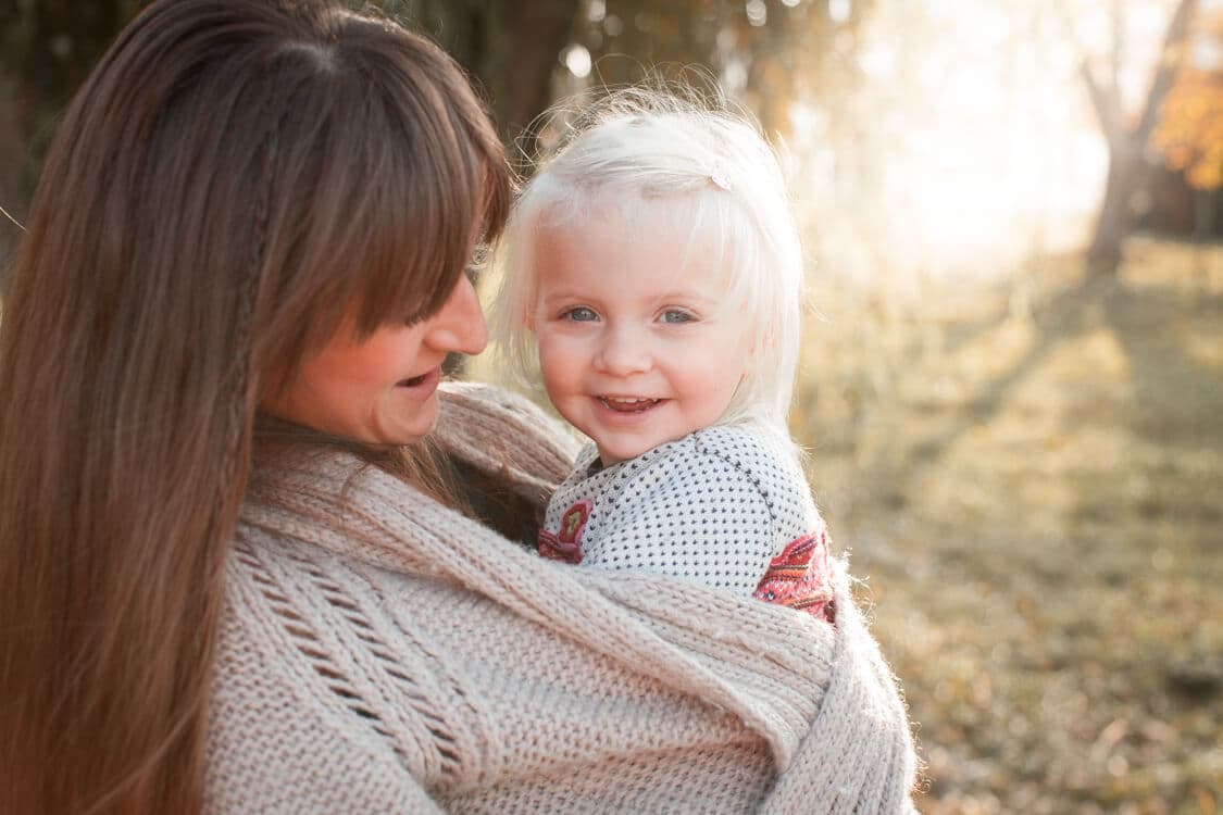 Kleines Mädchen im Strickmantel von der Mutter eingewickelt