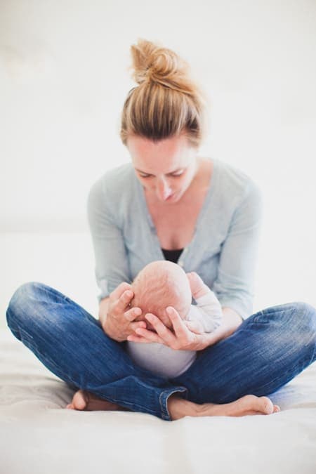 Mutter sitzt im Schneidersitz auf dem Bett und hält ihr Baby auf dem Schoß