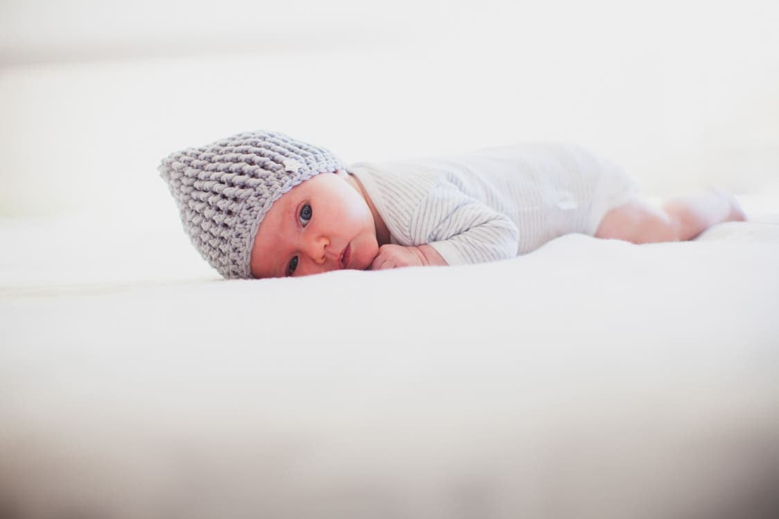 Baby mit Häkelmütze liegt auf dem Bauch
