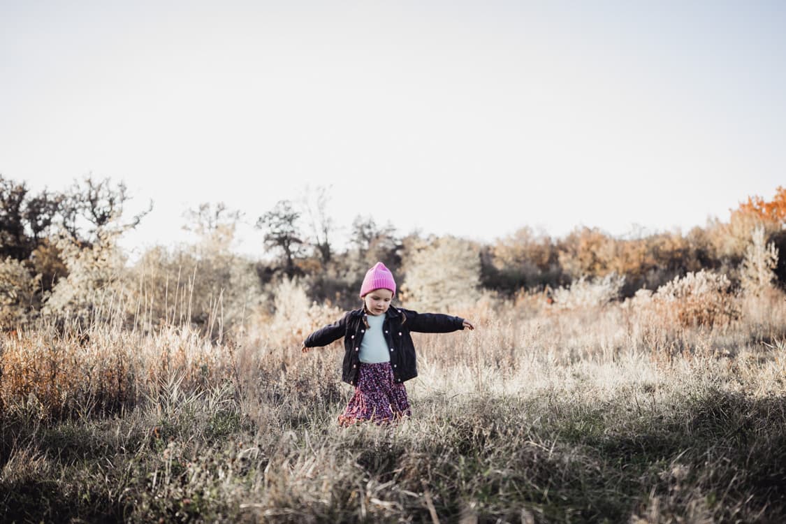 Maedchen laeuft mit ausgestreckten Armen ueber eine Wiese