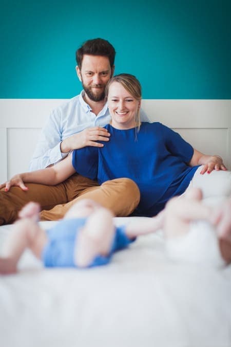 Eltern sitzen mit ihren Zwillingsbabys auf dem Bett und schauen sie an