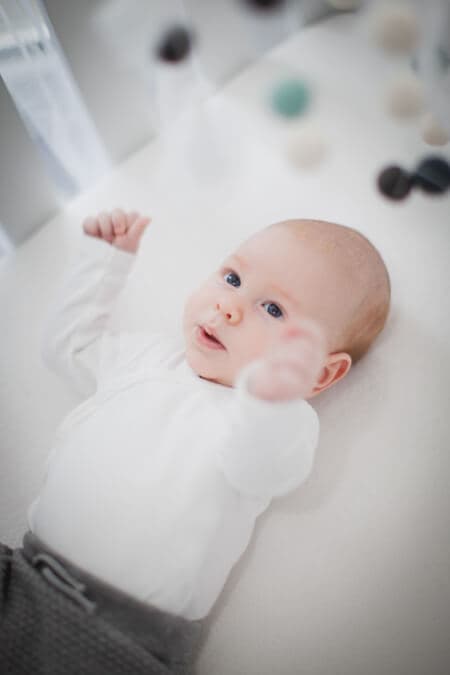 Baby liegt in seinem Bett. Darüber hängt ein Mobile.