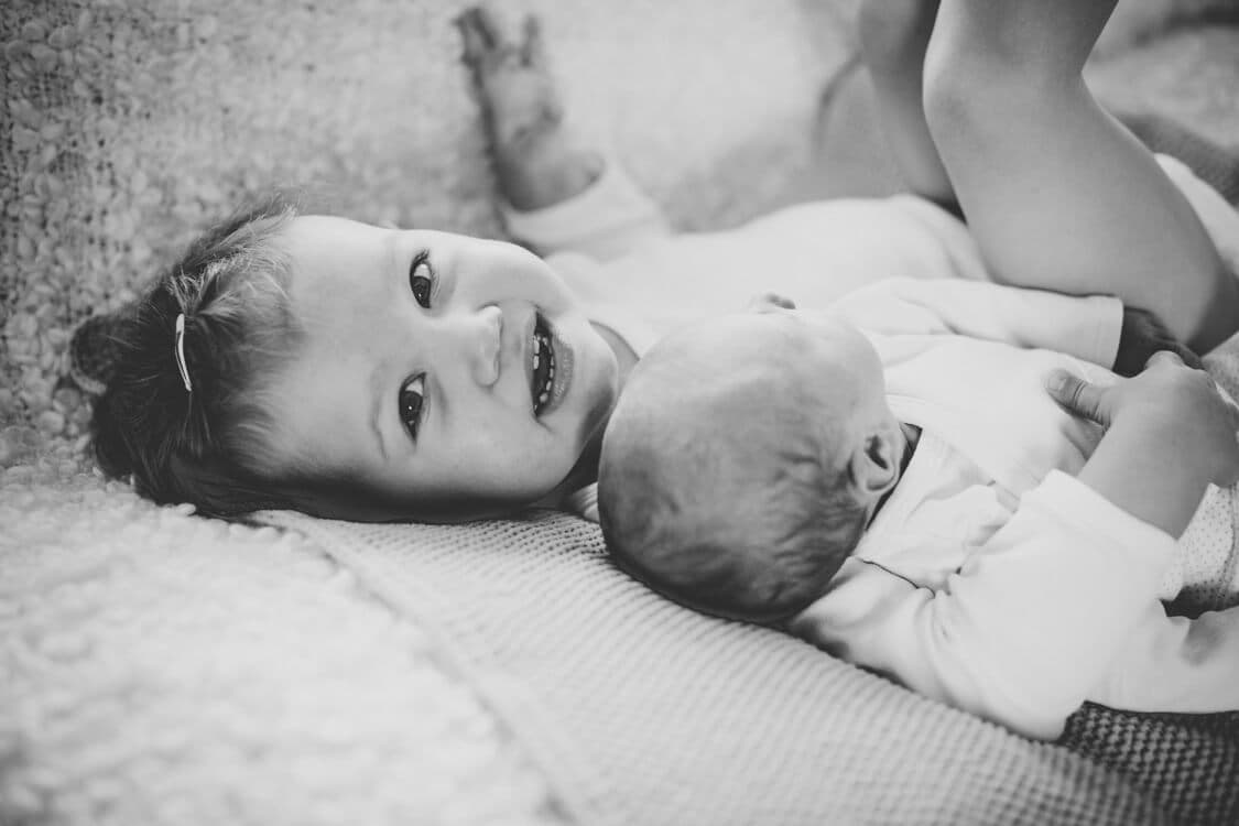 Kleines Mädchen liegt neben neugeborener Schwester