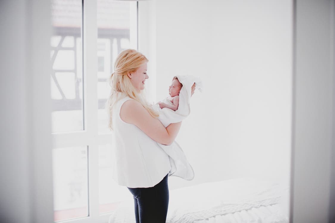 Mutter hält ihr vor sich auf dem Arm ihr Neugeborenens im Handtuch mit Kaputze