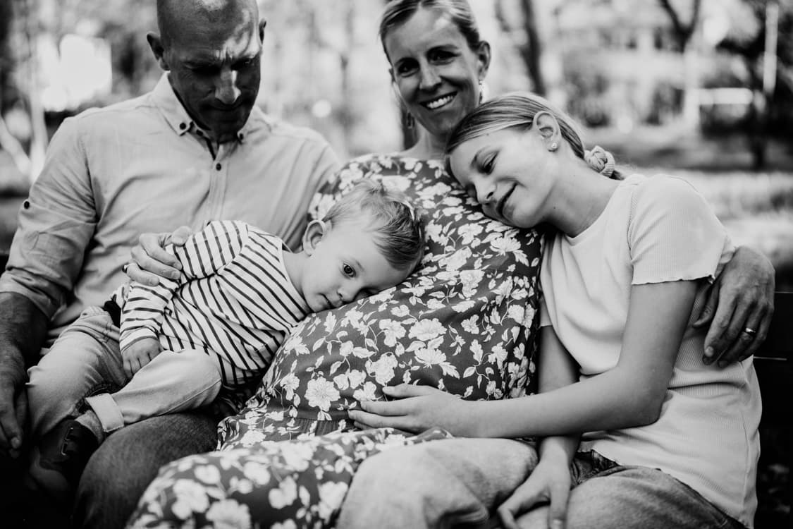 Familie sitzt auf einer Bank und kuschelt mit dem Babybauch der Mutter