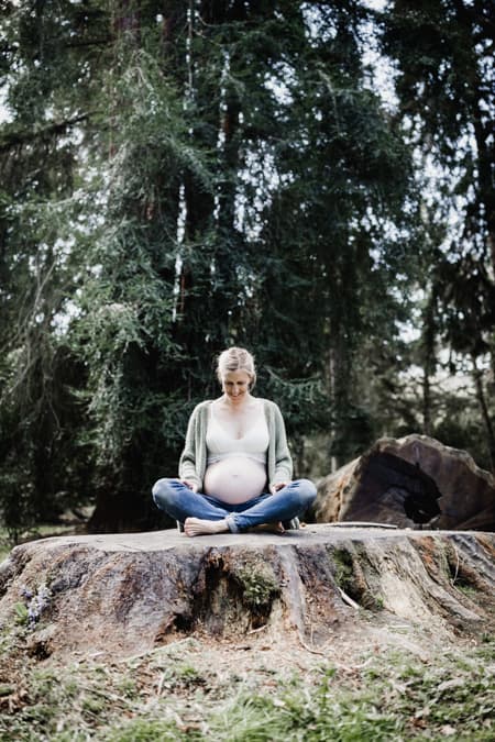 Schwangere Frau sitzt auf einem Baumstumpf