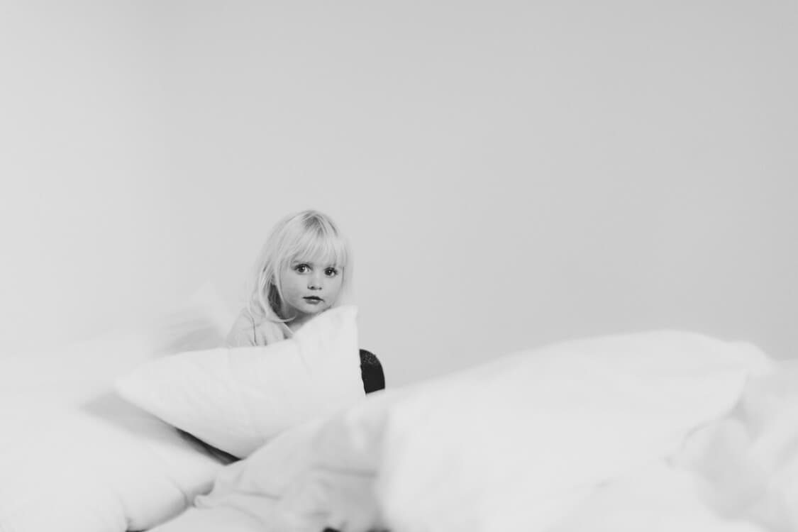 Mädchen sitzt auf Bett hinter vielen Kissen