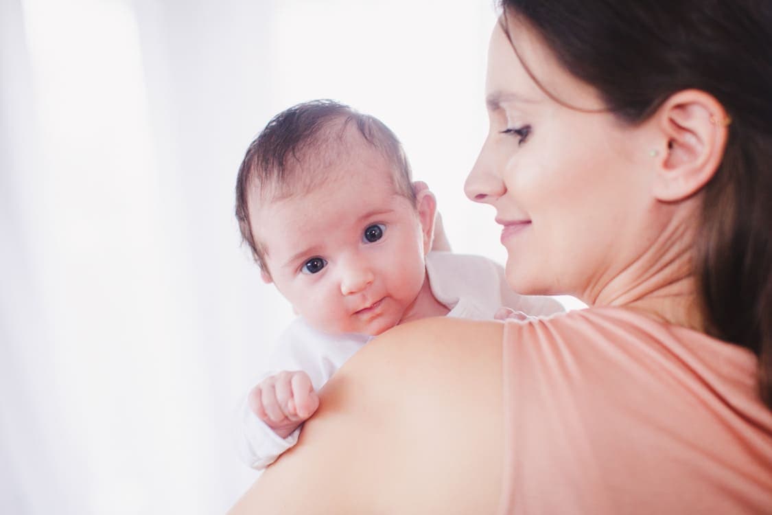 Baby guckt ganz wach über die Schulter der Mutter