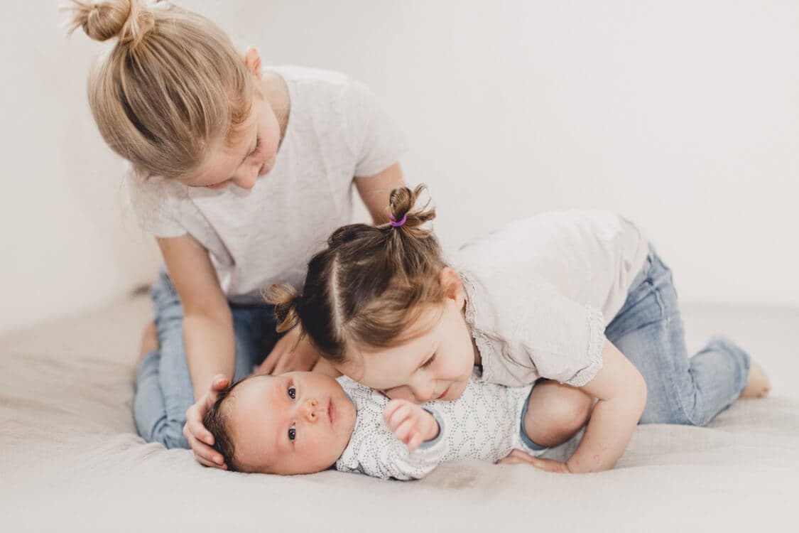 Schwestern beugen sich über ihren Bruder und kuscheln mit ihm
