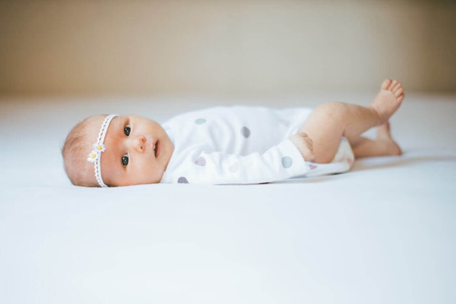 Baby mit Stirnband liegt auf einem Bett