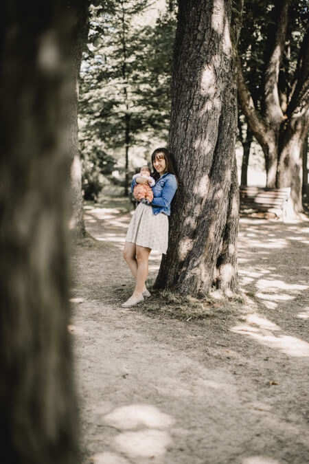 Frau mit Baby auf dem Arm vor einem Baum von weitem