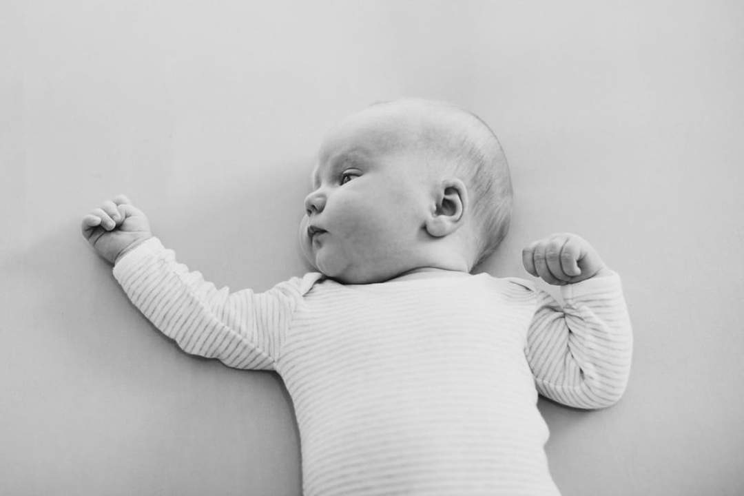 Baby liegt auf einer weißen Matraze und blickt zur Seite
