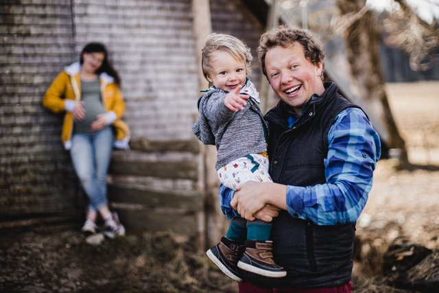 Mann mit Sohn auf dem Arm und Frau im Hintergrund