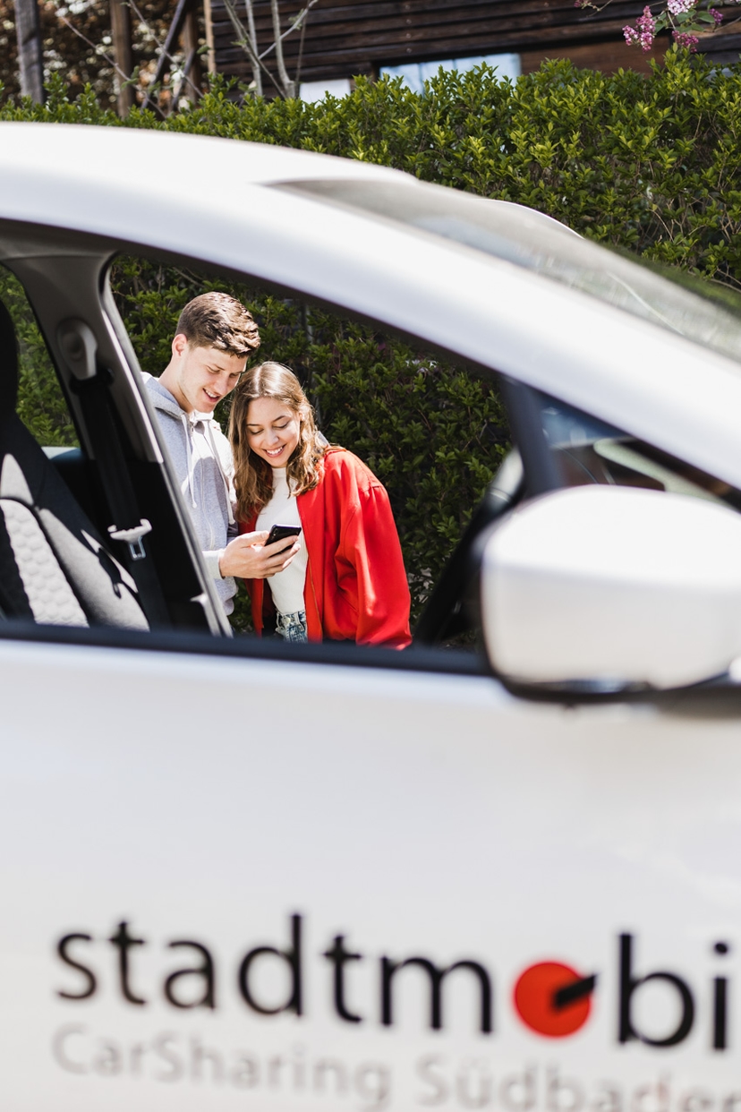 Junges Paar hinterm Auto schaut auf ein Handy