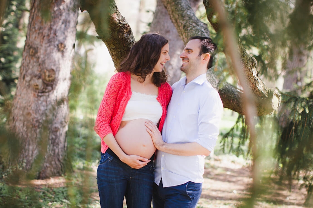 Schwangere Frau mit Mann stehen unter einem Baum und blicken sich in die Augen