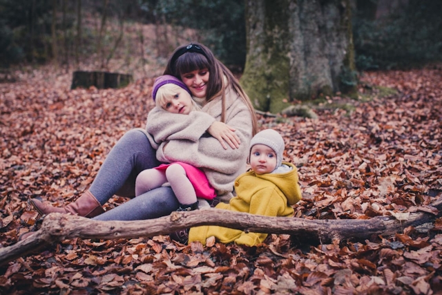 Mutter mit ihren Kindern sitzt auf dem Boden voller Blätter