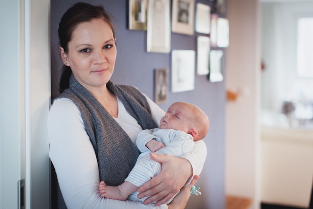 Frau mit Baby auf dem Arm lehnt an Türrahmen
