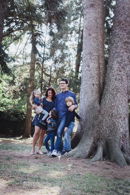 Familie mit drei Kindern steht vor einem Baum