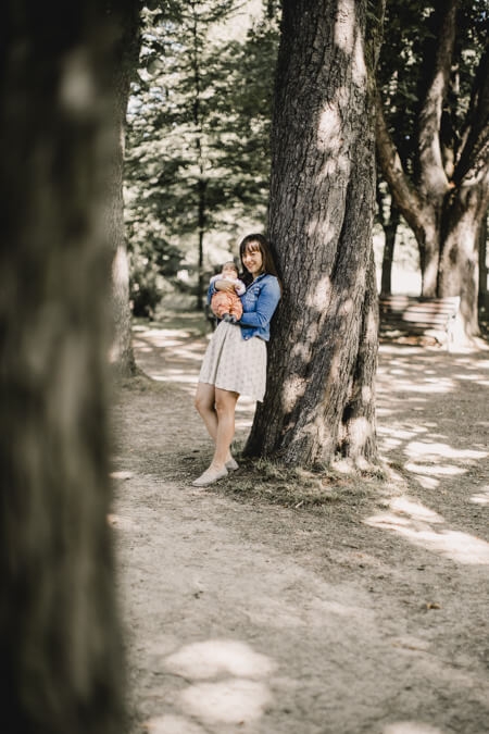 Frau mit Baby auf dem Arm vor einem Baum von weitem