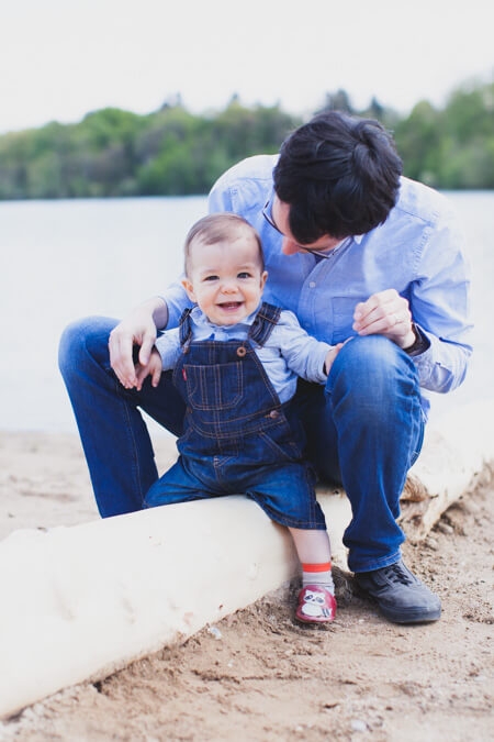Papa sitzt mit seinem kleinen Sohn am See auf einem Baumstamm