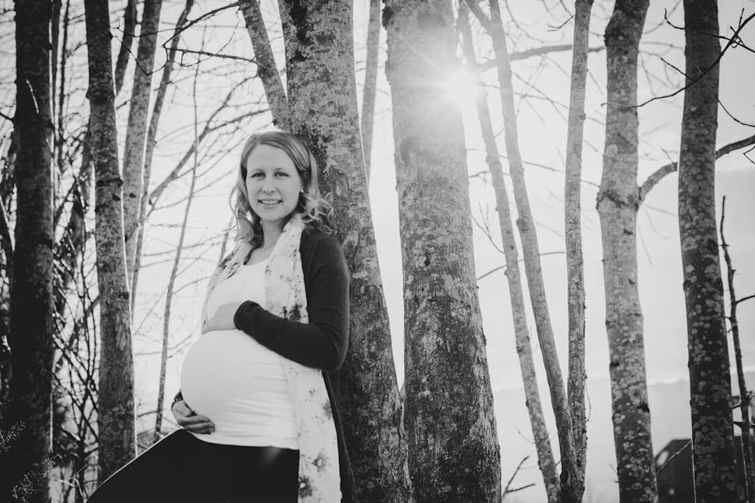 Schwangere Frau im Gegenlicht vor Baumstämmen
