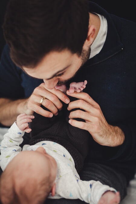 Vater küsst die Füße von seinem neugeborenen Sohn