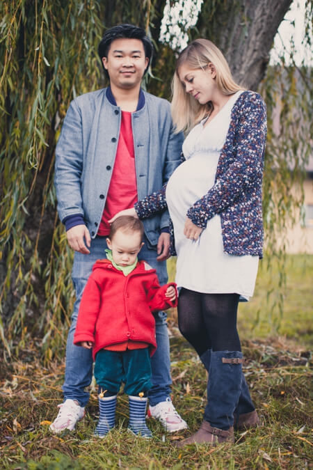 Kleine Familie mit schwangerer Frau steht unter einem Baum