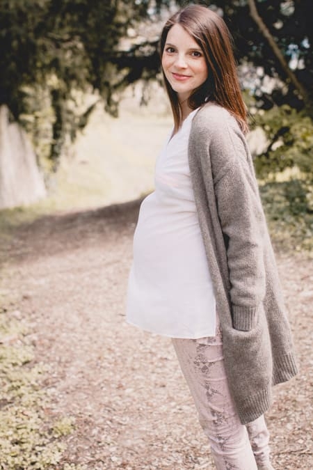 Schwangere Frau mit langem Strickmantel schaut über die Schulter