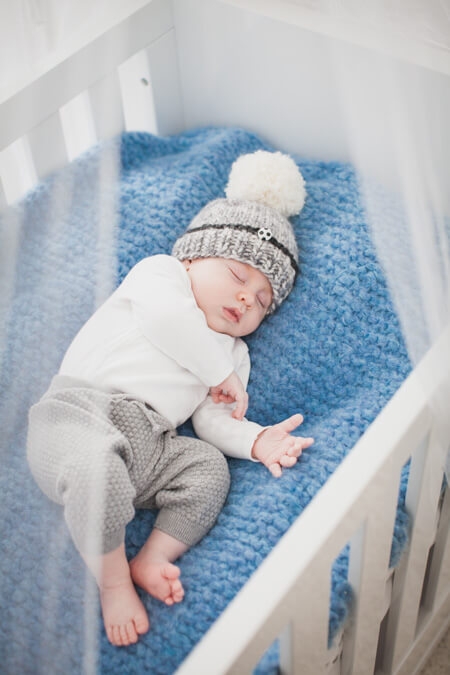 Baby schläft in seinem Babybett mit Mütze auf dem Kopf