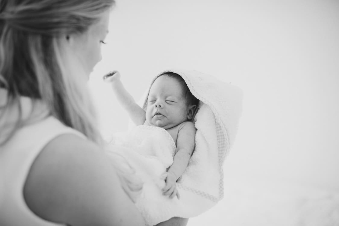 Neugeborenens im Handtuch mit Kaputze auf dem Arm der Mutter