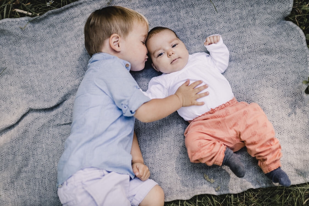 Baby liegt mit großem Bruder auf einer Decke. der Bruder gibt dem Baby einen Kuss.