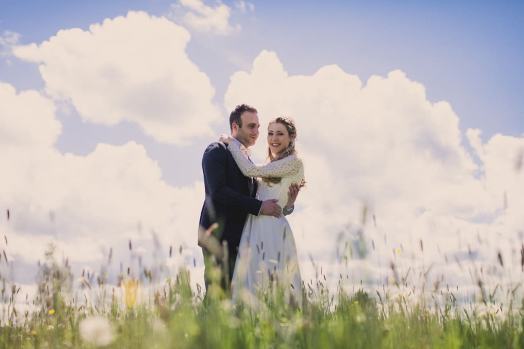 Brautpaar auf Wiese mit blauem Himmel und großen weißen Wolken
