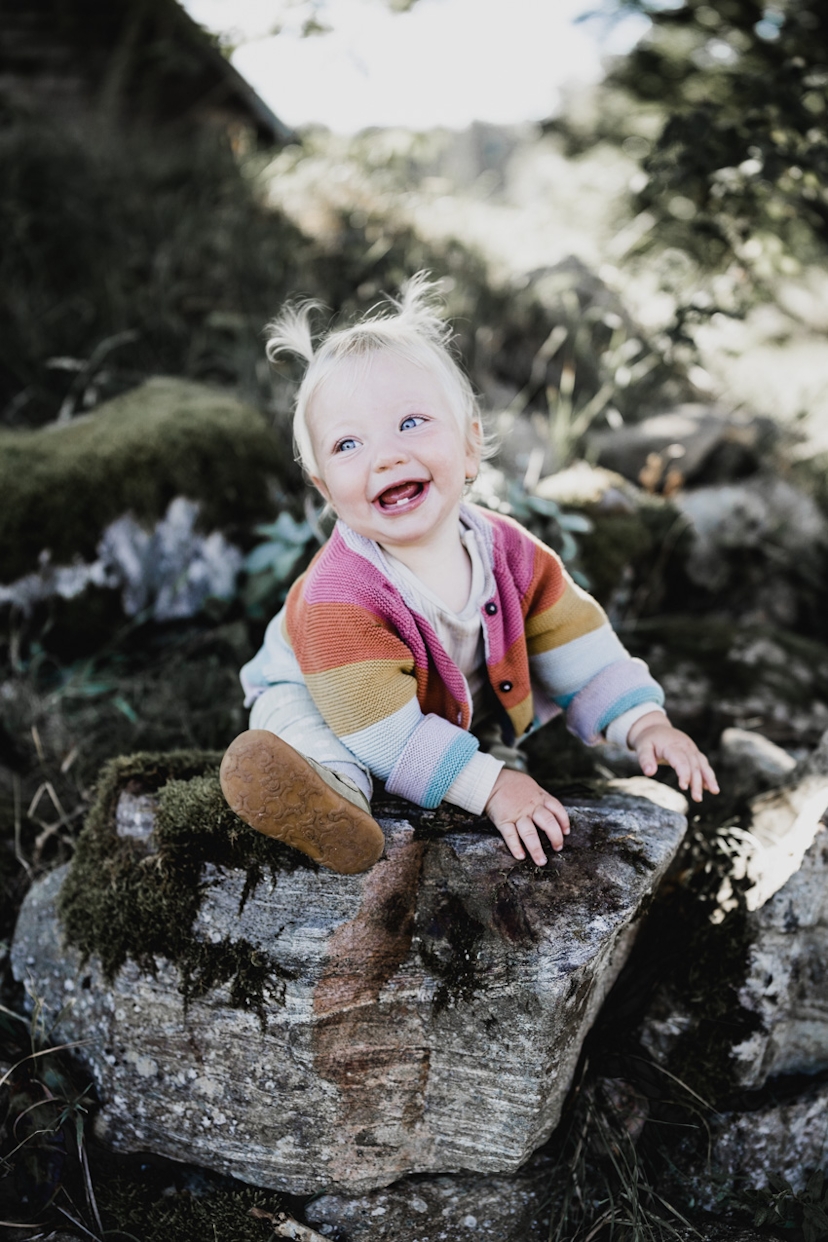 Kleines Mädchen sitzt auf einem Felsen und lacht